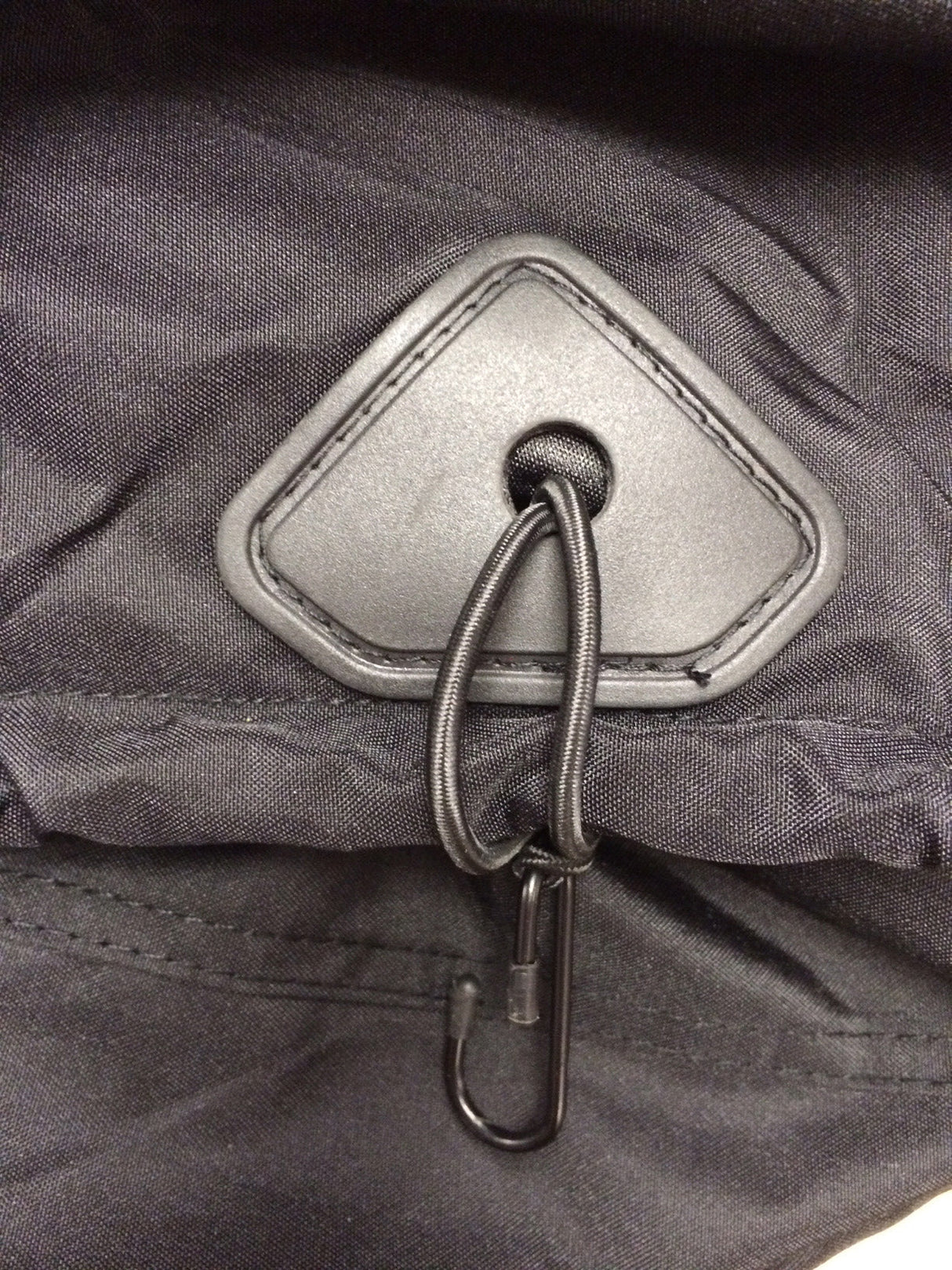 Close-up of lockable bottom hem on a black vehicle cover featuring reinforced grommet, elastic cord, and hook to secure the cover in place and prevent wind lift during outdoor storage.