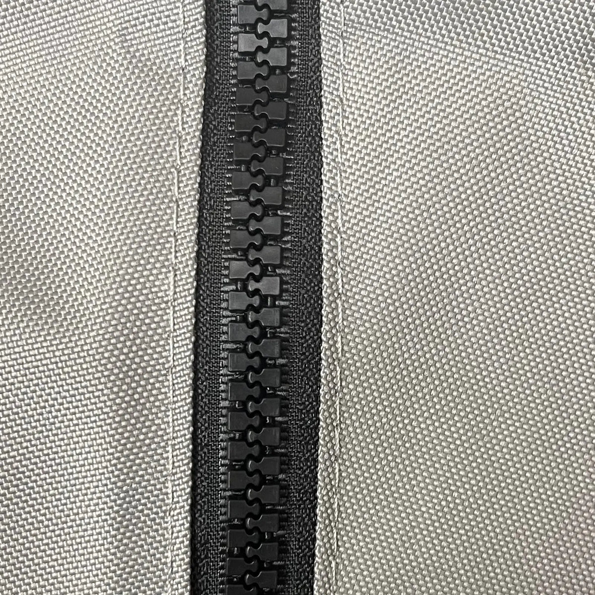 Close-up of heavy-duty black plastic zipper securely stitched on durable grey woven polyester fabric, showcasing weather-resistant, marine-grade construction for sailboat jib bags, designed for long-lasting outdoor performance and protection