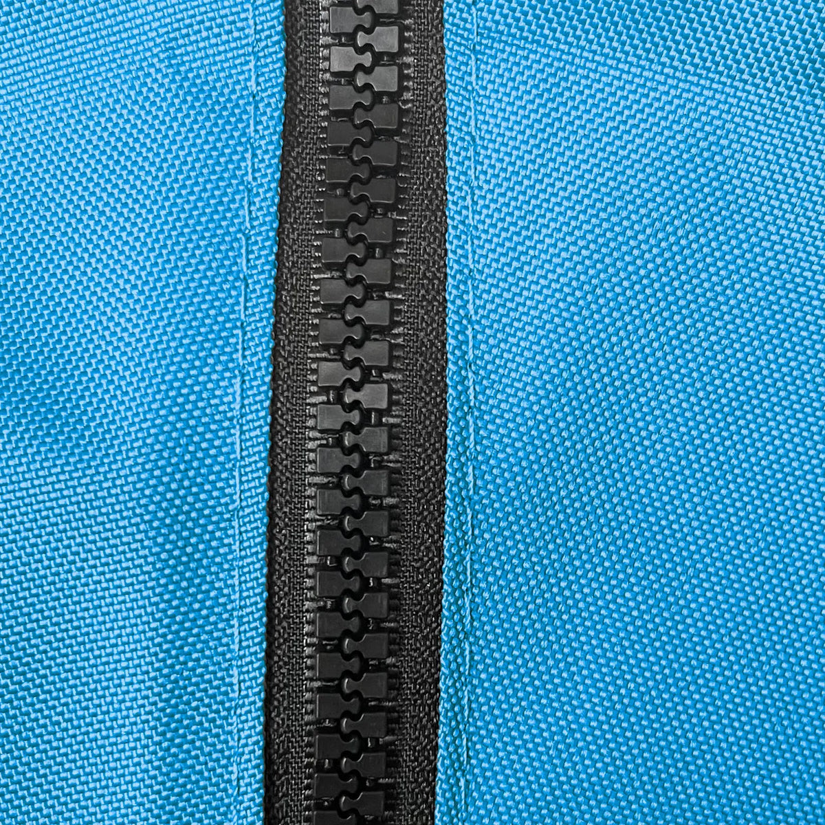 Close-up of heavy-duty black plastic zipper securely stitched on durable blue woven polyester fabric, showcasing weather-resistant, marine-grade construction for sailboat jib bags, designed for long-lasting outdoor performance and protection